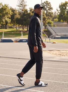 Ua Hovr Skyline Long Jump – A post-event recovery aesthetic featuring a branded oversized pullover hoodie, relaxed-fit nylon track pants, and a coordinated athletic baseball cap for a cohesive team-ready appearance.