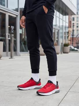 Ua Hovr Turbulence 2 – A streetwear-inspired outfit consisting of tapered black tech-fleece joggers, an oversized white graphic t-shirt, and a lightweight black windbreaker jacket.