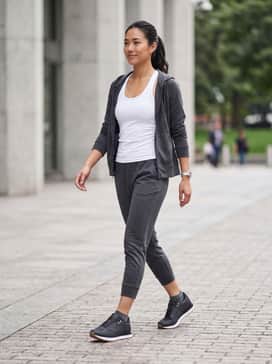 Ua Jogger – Tapered charcoal joggers paired with a fitted white racerback tank and a lightweight black zip-up hoodie for a cohesive gym-to-street look.