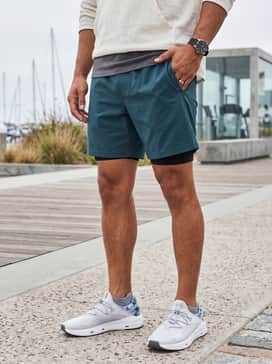 Ua Kilchis Camo – A relaxed beach-to-boardwalk ensemble with teal-colored swim trunks, a light grey heathered tank top, and polarized aviator sunglasses.