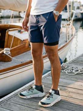 Navy blue tailored swim trunks and a crisp white linen shirt left unbuttoned over a grey heather tank top for a stylish boat outing.