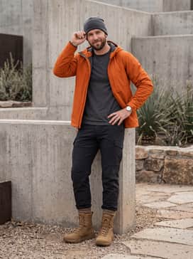 Ua Loadout Tactical – A modern technical look with black tapered hiking trousers, a bright orange waterproof shell jacket, and a charcoal performance beanie.