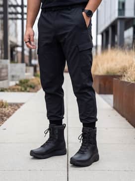 Ua Loadout Waterproof – Black tapered technical joggers with an oversized heavyweight hoodie and a long-line waterproof shell jacket for a futuristic urban techwear aesthetic.