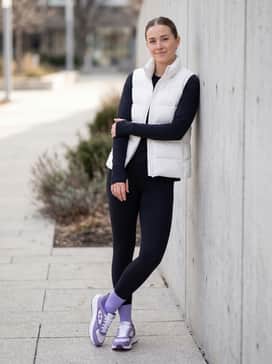 Ua Mirage Sport – Black high-performance leggings and a matching long-sleeve tech top, topped with a white puffer vest for a functional outdoor workout outfit.