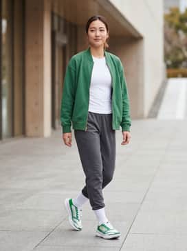 Tapered charcoal grey joggers paired with a fitted white compression shirt and an unzipped green collegiate-style bomber jacket.