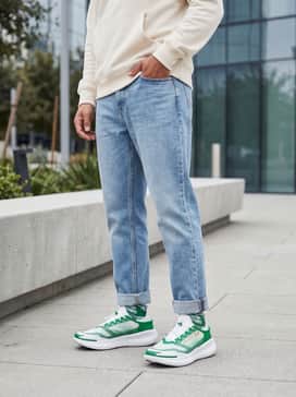 Light-wash relaxed jeans with the cuffs rolled up, a minimalist cream-colored hoodie, and a matching green baseball cap for a coordinated streetwear look.