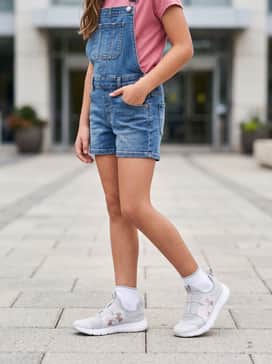 Ua Outhustle 2 Slip – A casual weekend ensemble consisting of medium-wash denim overall shorts worn over a rose-pink graphic t-shirt to highlight the shoe's logo color.