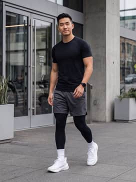 Ua Reign Xt – Black performance compression tights worn under charcoal grey mesh training shorts, paired with a fitted black moisture-wicking T-shirt and white crew socks.