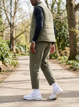 Olive green cargo-style training joggers with a black long-sleeve compression base layer and a lightweight black quilted gilet for an outdoor training session.