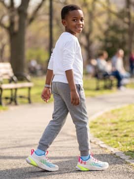 Black jogger-style sweatpants with a simple white long-sleeve shirt and a bright pink baseball cap to tie the shoe's heel-pull color into the ensemble.