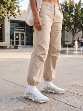 Ua Sculpt Trainer – Beige wide-leg cargo pants with cinched ankles, a cropped white baby tee, and a neutral-toned baseball cap for an urban streetwear vibe.