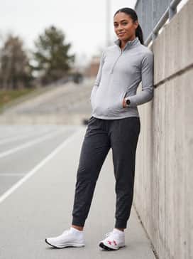 Full-length charcoal grey compression tights worn with a fitted grey quarter-zip pullover and a minimalist sports watch for professional warm-up sessions.