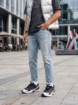 Ua Sola – Straight-leg distressed light-wash denim, an oversized charcoal graphic t-shirt, and a metallic silver puffer vest for a high-contrast look.