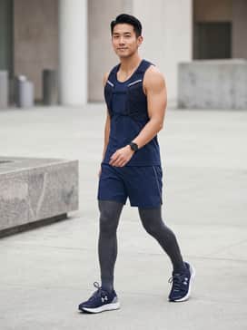 Ua Speedform Gemini – A high-performance look featuring charcoal grey compression leggings, a moisture-wicking navy blue racerback tank, and a lightweight reflective running vest for early morning visibility.