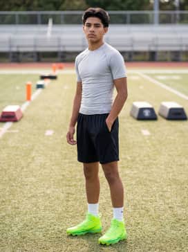 Ua Spotlight Hammer Jr – A professional practice ensemble consisting of black moisture-wicking mesh shorts, a light grey tech-fabric compression shirt, and white crew-length performance socks.