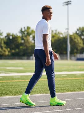 Ua Spotlight Hammer Jr – A field-side training outfit including navy blue perforated shorts, a white graphic sports t-shirt with lime green logos, and a matching athletic cap.
