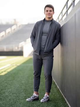 Ua Spotlight Pro Click Clack – A sleek charcoal grey technical track suit with a zip-up jacket and tapered joggers, ideal for sideline warm-ups and post-game travel.