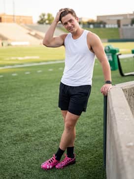 Ua Spotlight Pro Pth – All-white practice gear including a moisture-wicking tank and ventilated shorts to make the vibrant pink cleats the focal point of the outfit.