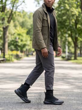 An urban utilitarian style pairing slim-fit charcoal chinos with a black quarter-zip performance fleece and a structured olive drab field jacket for a clean yet functional aesthetic.