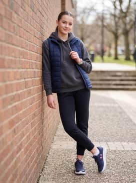 Ua Surge – Tapered black joggers combined with a charcoal grey hoodie and a lightweight quilted vest to create a comfortable and stylish outfit for errands or travel.