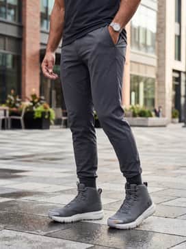 Ua Valsetz Mid – Tapered dark indigo denim jeans with a slight cuff, a grey heathered sweatshirt, and a black nylon bomber jacket for a modern, city-ready look.