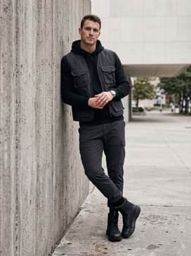 Dark charcoal utility workwear denim paired with a fitted black hoodie and a tactical vest for a modern, rugged urban ensemble.