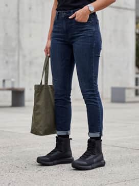 Dark-wash tapered jeans with a slight cuff above the boot collar, styled with an oversized olive green field jacket and a minimalist black backpack.