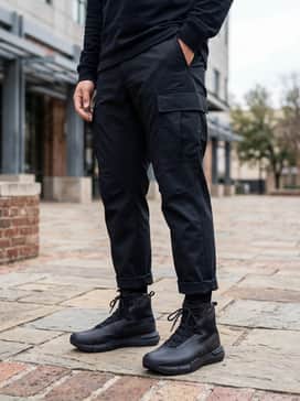 A rugged utility outfit comprising dark indigo straight-leg denim jeans cuffed to show the boot's collar, paired with a heavy-duty black thermal shirt and an olive green field jacket.