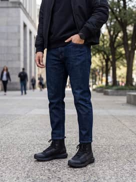 Dark indigo utility denim jeans with a slight taper at the ankle, an oversized black graphic hoodie, and a matte black bomber jacket for a modern techwear aesthetic.