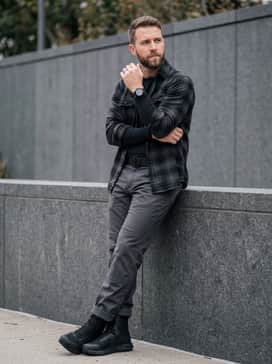 Rugged charcoal straight-leg work trousers with a heavy-duty nylon belt, paired with a durable flannel shirt layered over a black compression base layer.