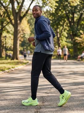 Ua Velociti Elite 3 – Athleisure Recovery: Tapered black performance joggers worn with a fitted slate grey technical tee and a lightweight navy windbreaker for a post-workout look.