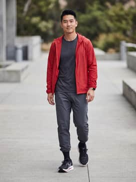 A full performance kit including black compression leggings, a moisture-wicking charcoal technical tee, and a lightweight red windbreaker to match the midsole accents.