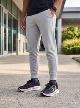 A street-ready athleisure look with tapered tech fleece joggers in light grey, a crisp white oversized hoodie, and a black nylon baseball cap.
