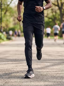 Ua Velociti Pro 2 – A casual weekend outfit featuring slim-fit black chinos cuffed at the ankle, a premium grey crewneck sweatshirt, and a minimalist black technical backpack.