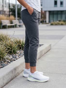 Ua Velociti Spd – Tapered charcoal tech-fleece joggers, a crisp white moisture-wicking performance tee, and a sleek black utility vest for a functional urban commute.