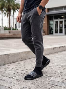 A post-gym recovery look with charcoal grey tapered tech fleece joggers, a black breathable muscle tank, and a sleek waterproof sports watch.