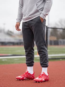 Dark charcoal tapered fleece joggers paired with a light grey moisture-wicking hoodie and a red snapback cap for a coordinated post-game aesthetic.