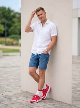 A relaxed summer outfit pairing medium-wash denim shorts with a white linen short-sleeve button-up shirt and red-accented crew socks.