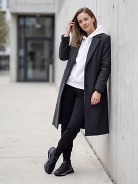 Tapered black tech-fleece trousers with a white oversized hoodie and a long wool topcoat for a sophisticated fusion of sport and luxury.