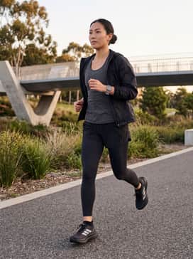 A professional athletic look featuring black compression leggings, a charcoal moisture-wicking racerback tank, and a lightweight silver windbreaker.