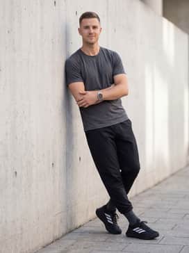 A casual weekend outfit pairing slim-fit black denim, a heather grey hoodie, and a utility vest in an olive or navy tone.
