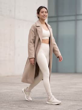 Cream-colored high-waisted leggings paired with a matching sports bra and a beige oversized trench coat for a sophisticated monochrome gym-to-street transition.