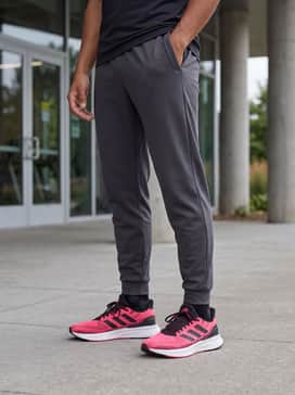 A sleek gym ensemble comprising charcoal grey tapered joggers, a black sleeveless muscle hoodie, and high-performance crew socks that peak just above the ankle to keep the focus on the vibrant footwear.