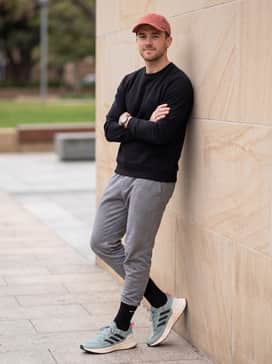 A weekend-ready athleisure ensemble featuring slim-fit grey joggers, a simple black crewneck sweatshirt, and a coral-colored baseball cap to pop the shoe's accents.