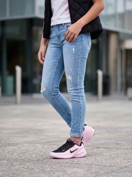 Distressed light-wash denim skinny jeans with a graphic white t-shirt featuring pink accents and a black quilted vest for a stylish school day outfit.