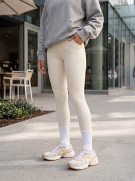 High-waisted cream leggings and a matching sports bra, layered with an oversized heather grey hoodie and tall white crew socks pulled over the leggings.