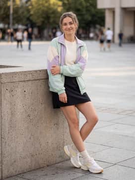 A black nylon mini skirt with a tucked-in graphic baby tee and a vintage-style windbreaker in pastel tones.