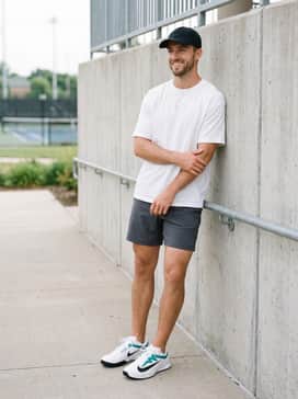 A modern athleisure ensemble with charcoal grey performance shorts, a breathable white oversized tee, and a black baseball cap.