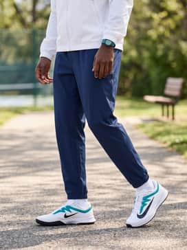 A sporty casual weekend fit pairing navy blue track pants with a white zip-up windbreaker and a teal-accented sports watch.