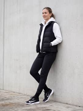 A sporty athleisure ensemble pairing black technical joggers with a fitted white hoodie and a sleek black puffer vest for cooler outdoor practice sessions.